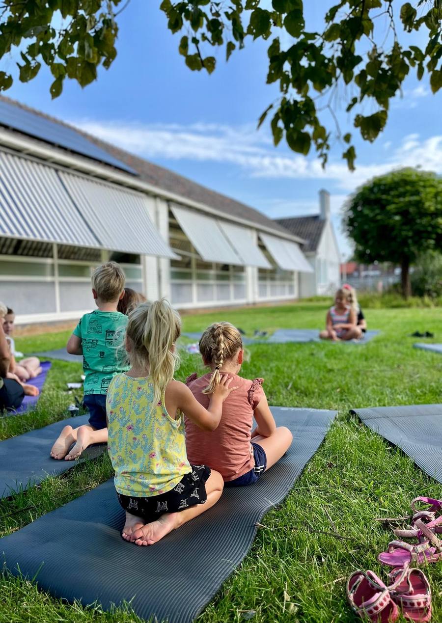 Kinderen zitten op yogamatten in het gras tijdens een buitenles